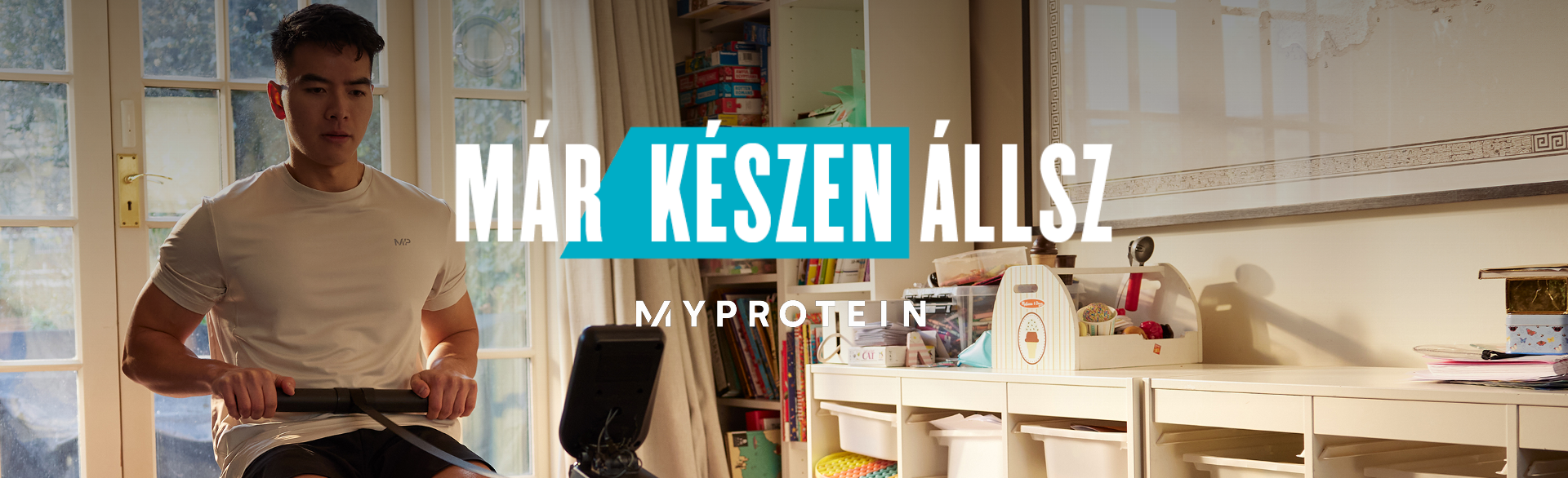 Egy férfi edz egy otthoni evezőgépen, rajta a "Már készen állsz - MYPROTEIN" felirat.