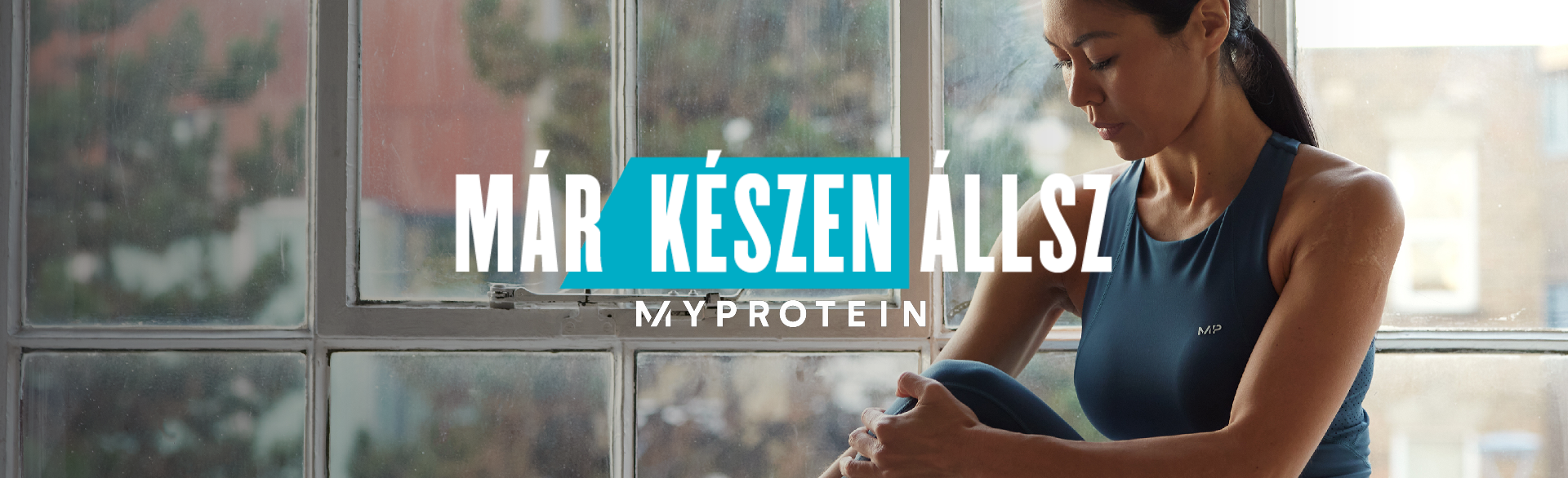 Egy MP edzőtermi ruhát viselő nő ül egy ablakpárkányon és nyújtózkodik, a kép fölött a "Már készen állsz - MYPROTEIN" szöveggel.